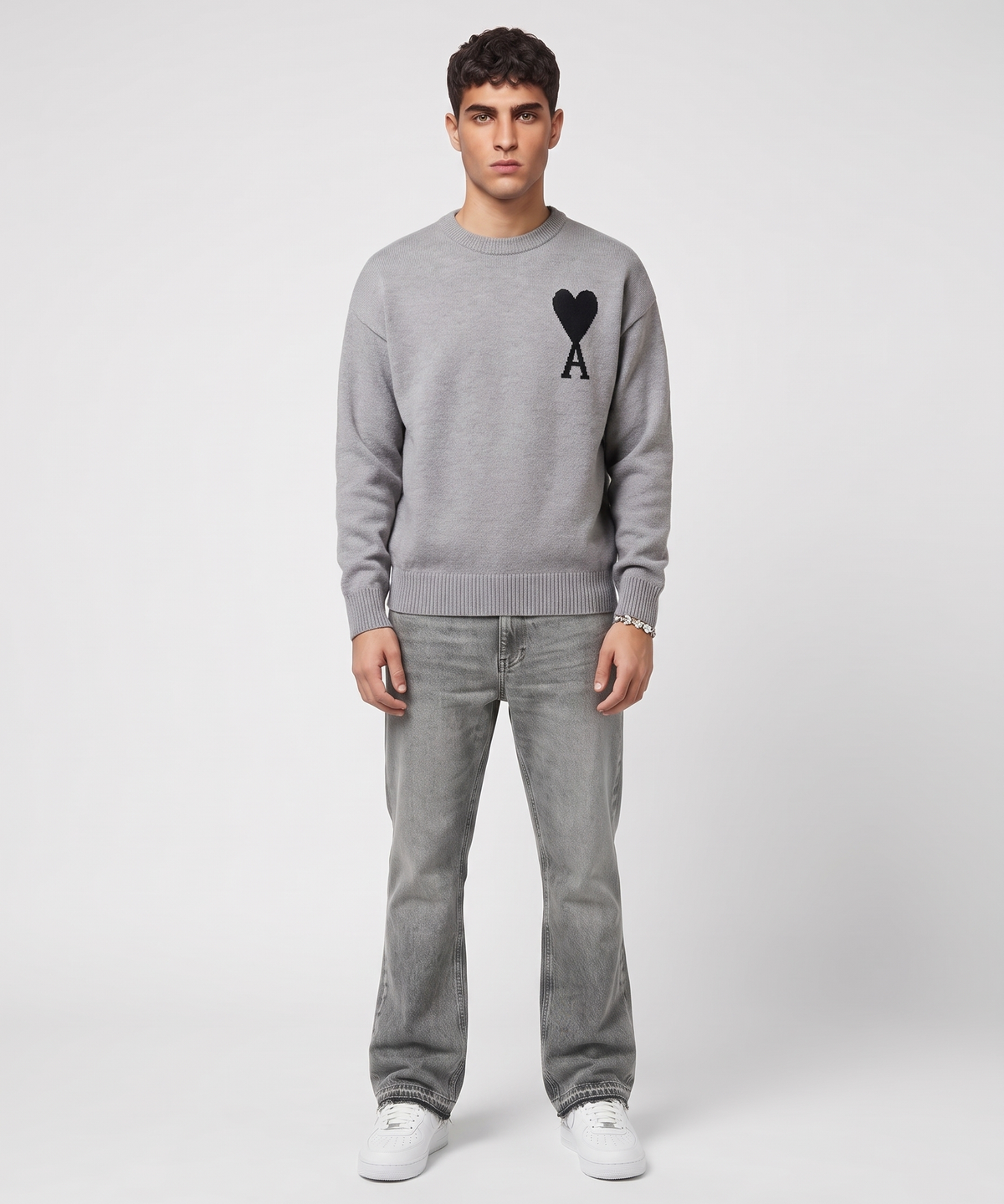 Model trägt den grauen Sweater mit schwarzem Herz-Logo, graue Bootcut-Jeans, weiße Sneaker und Armband